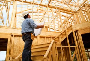 Construction worker with blueprints inside wood framed house.